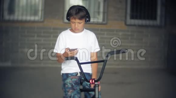 男孩坐在BMX自行车上听智能手机上的音乐视频的预览图