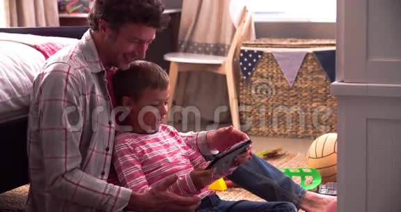 父亲和儿子使用数码平板电脑坐在卧室视频的预览图