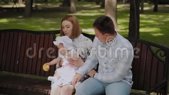 快乐的年轻家庭他的儿子在夏天在公园里的长凳上休息一个漂亮的女人和她的丈夫视频的预览图