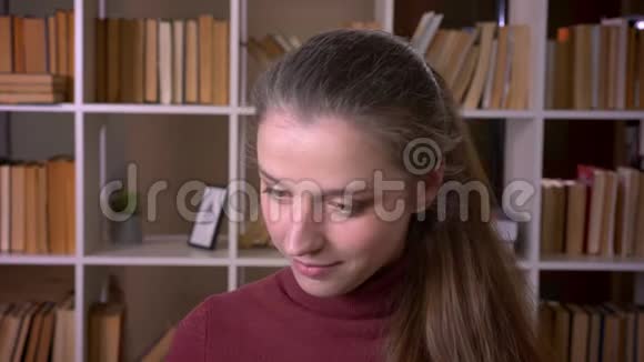 一幅年轻的白种人女学生的特写照片她开心地笑着看着室内图书馆的摄像机视频的预览图