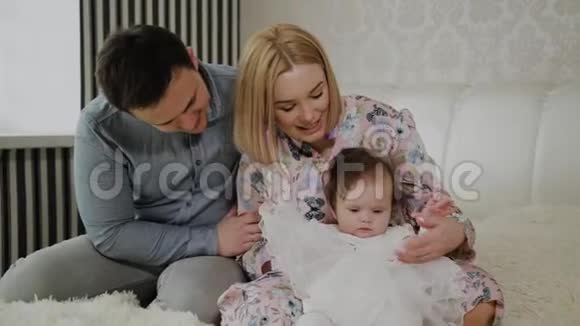幸福的家庭在白色的床上和他们的小女儿玩耍视频的预览图