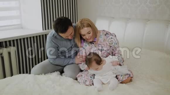 幸福的家庭在白色的床上和他们的小女儿玩耍视频的预览图