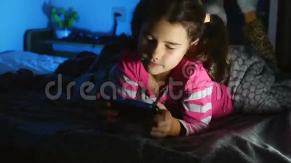 一个女孩在室内玩手提电子游戏一个晚上玩游戏机的孩子视频的预览图