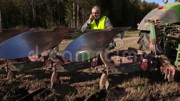 农夫在拖拉机旁用犁打电话视频的预览图