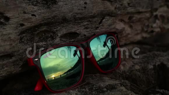 太阳落山时太阳镜躺在沙滩上戴着墨镜反射着大海海浪和天空视频的预览图