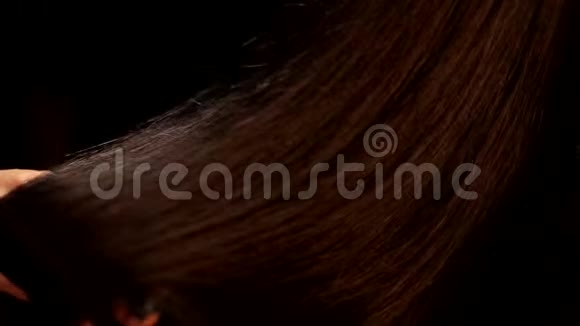 特写黑色背景镜头女性手旋转美丽的直巧克力深色闪亮的头发视频的预览图