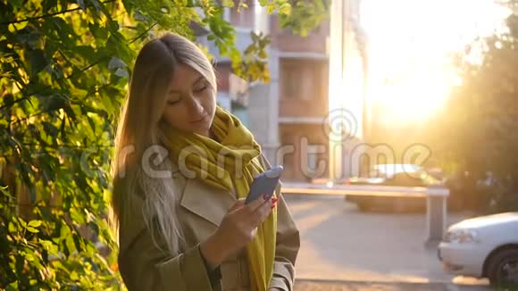 一位美丽的年轻女子的肖像她在城市里散步时享受秋天穿着雨衣的漂亮金发女郎视频的预览图