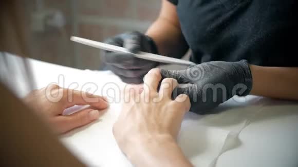 美容师在美甲沙龙中将指甲油涂在女性指甲上的特写镜头女性指甲修剪水疗视频的预览图