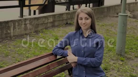 美丽的女孩坐在城市公园的长凳上视频的预览图
