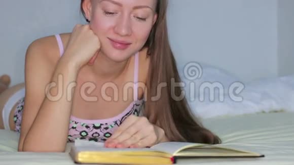 美丽的女孩躺在床上看书视频的预览图