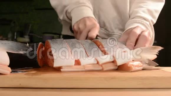 女性手的特写用刀子切一大条鲑鱼放在木制的家庭烹饪桌上视频的预览图
