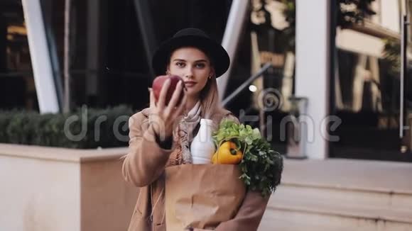 年轻漂亮的女人穿着时髦的外套站在街上手里拿着一包产品微笑着看着视频的预览图