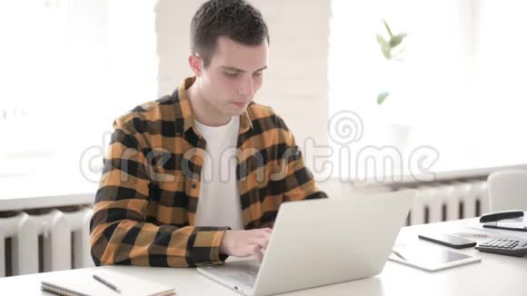 头痛的休闲青年在笔记本电脑上工作视频的预览图