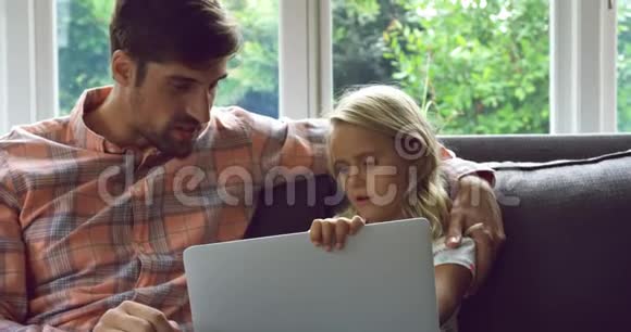 父亲和女儿在家里沙发上用笔记本电脑视频的预览图