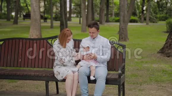 快乐的年轻家庭他的儿子在夏天在公园里的长凳上休息一个漂亮的女人和她的丈夫视频的预览图