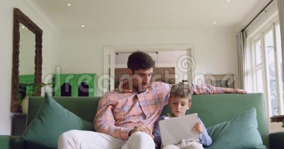 父亲和儿子在家里的沙发上用数码平板电脑视频的预览图