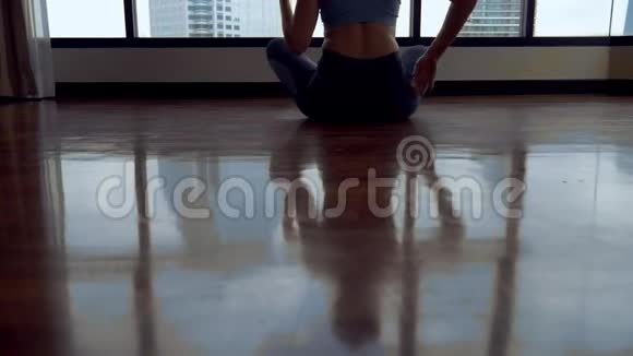 年轻女子在一个房间里做瑜伽靠近一扇大窗户俯瞰摩天大楼视频的预览图
