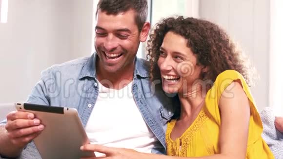 可爱的情侣在沙发上用平板电脑视频的预览图
