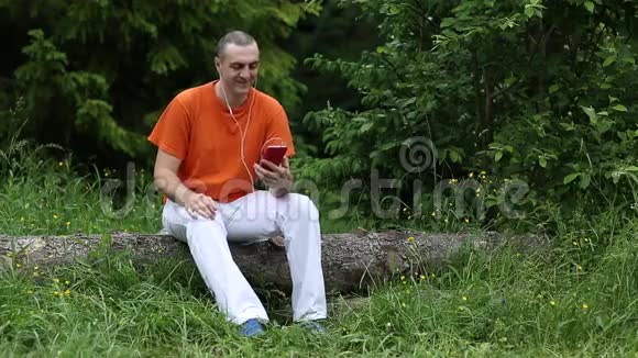 有智能手机的人坐在森林中的一棵倒下的树上视频的预览图