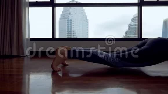 年轻女子在一个房间里做瑜伽靠近一扇大窗户俯瞰摩天大楼视频的预览图
