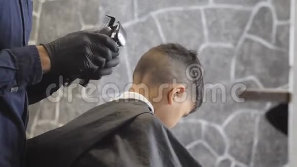 戴着黑手套的理发师仔细地把一个在理发店工作的亚洲小孩的头发剃成60英尺高的形状视频的预览图