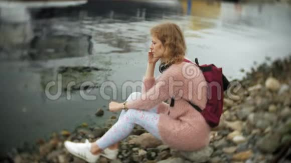 一个女孩在海滩上使用智能手机用耳机听音乐跳舞游艇在港口航行视频的预览图
