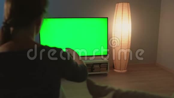 女人坐在沙发上用绿色屏幕看电视用遥控器切换频道彩色键视频的预览图
