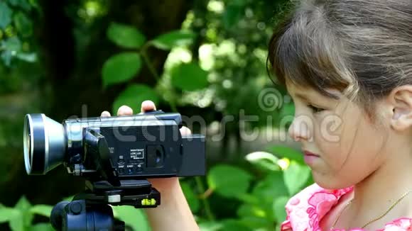 年轻女孩在绿色公园背景下看摄像机视频的预览图