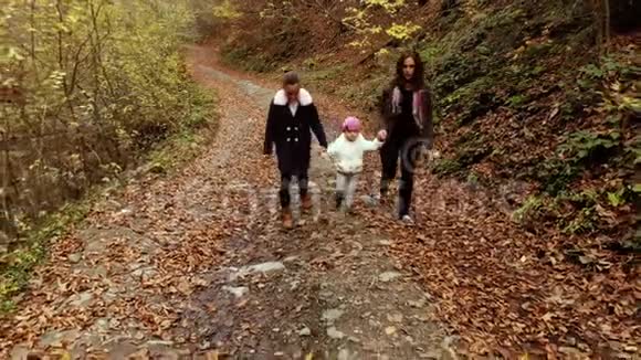 一位年轻的母亲带着她的两个孩子走过秋天的森林他们沿着森林小径走他们很开心视频的预览图