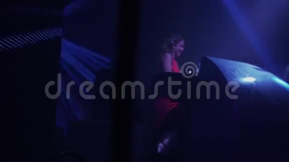 戴着耳机的女孩穿着红色连衣裙在夜总会的转盘上表演聚光灯视频的预览图