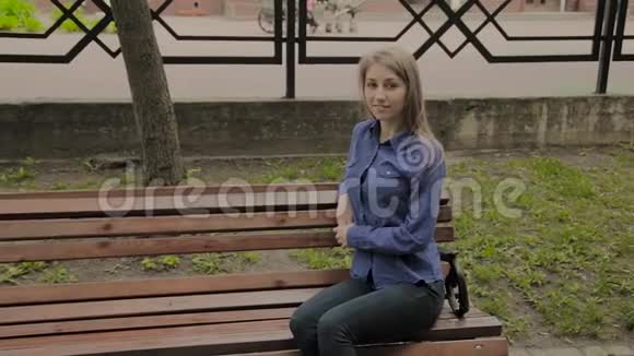 美丽的女孩坐在城市公园的长凳上视频的预览图