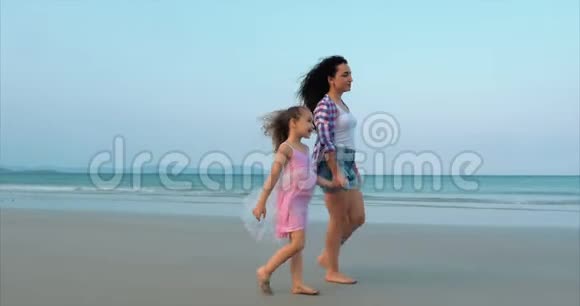 年轻的家庭母亲和女儿正沿着海岸散步幸福的家庭在海边散步视频的预览图
