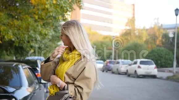 一位美丽的年轻女子的肖像她在城市里散步时享受秋天穿着雨衣的漂亮金发女郎视频的预览图