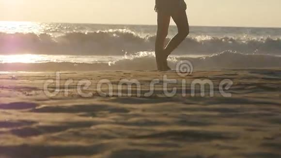 年轻女子踩在沙滩上的腿靠近女性的脚在沙滩上金色的沙滩上行走海浪在视频的预览图