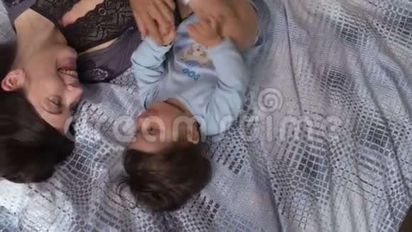 怀孕的母亲和她的小儿子躺在卧室的床上玩耍玩得很开心亚裔混血儿男孩视频的预览图