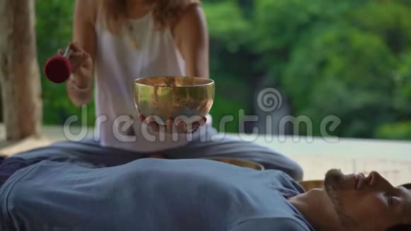 一位亚洲圣药大师为一位年轻的客户表演藏碗治疗仪式的女子拍摄的超慢镜头视频的预览图