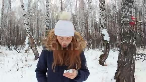 那个女孩带着电话在冬天的树林里散步视频的预览图