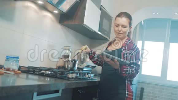 女人在厨房煮汤防止锅中的水看看数字平板上的食谱妇女视频的预览图
