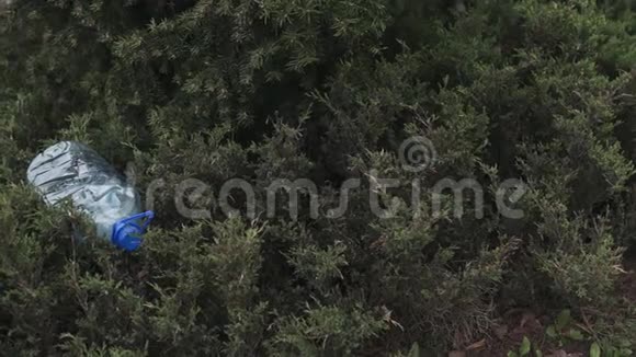 蓝色的大塑料瓶躺在公园森林里的树上扔出不回收的垃圾和污染视频的预览图