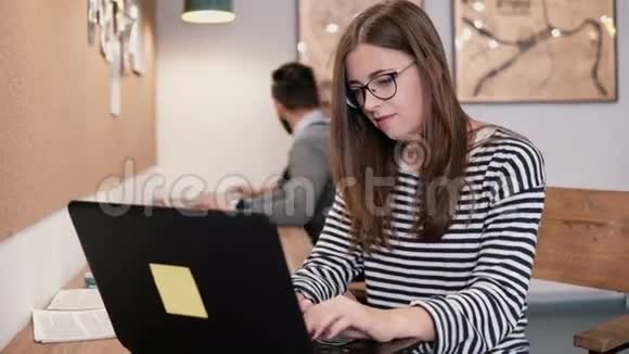 年轻漂亮的女孩在现代的创业办公室里用笔记本电脑工作视频的预览图