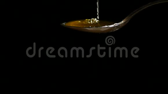 从黑色背景上的不锈钢茶匙滴下的蜂蜜视频的预览图