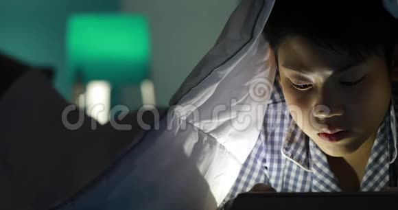 小男孩在床上玩手机或智能手机夜晚视频的预览图