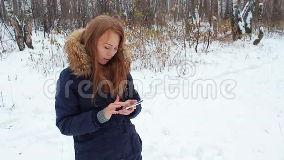 那个女孩带着电话在冬天的树林里散步视频的预览图