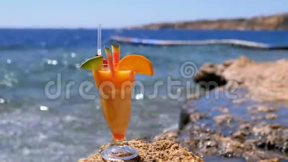埃及海滩上的一个装有稻草的玻璃杯中的热带新鲜果汁矗立在海边的岩石上视频的预览图