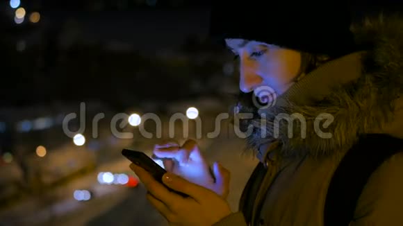 年轻漂亮的女人晚上在城里用智能手机视频的预览图