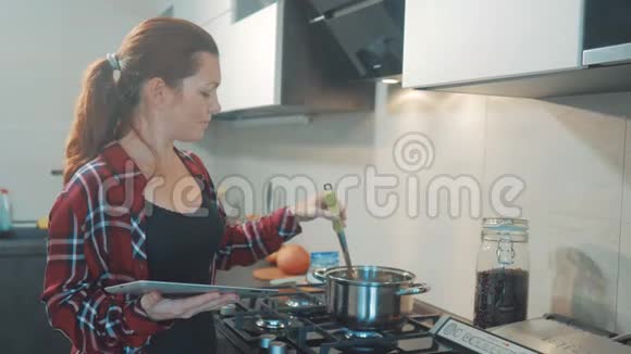 女人在厨房煮汤锅防止锅里的水看看数字平板上的食谱妇女视频的预览图