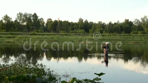 渔夫在一条平静的河里钓鱼一个穿着渔具的人在河里站着扔一根鱼竿视频的预览图