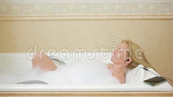 美丽的女人洗澡听耳机上的音乐手机视频的预览图