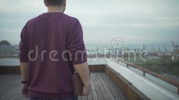 一个身穿便服手拿日记的深色头发的男人看着阴天在木顶上行走的海港海景视频的预览图