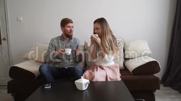 夫妻俩坐在家里的沙发上喝着白茶看着电视视频的预览图